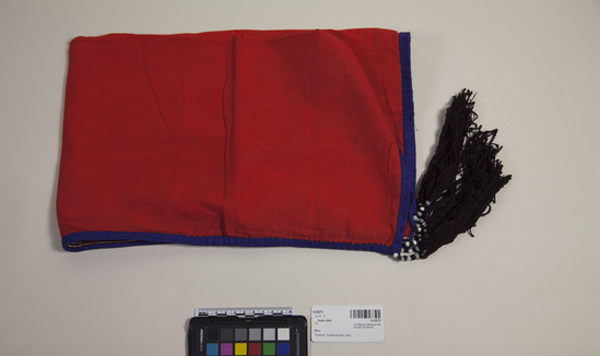 Hearst Museum object titled Head cloth, accession number 9-23275, described as Red cloth for wedding hat. Light linen cloth dyed red. Trimmed on three edges with thin appliqué stripes of blue, red, white and brown. Final edge trimmed in blue. Two brown tassels at each corner. Tassels hang from strings of beads.