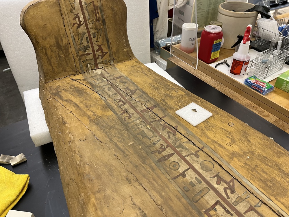 Hearst Museum object 13 of 167 titled Coffin, accession number 6-19912, described as Wooden anthropoid coffin. Inscription running down center of lid. Determined by Kea Johnston to probably be the outer coffin of Iwefaa (6-19928, 12-11039). According to Kea Johnston, "This coffin belonged to a man named Iwefaa, whose name is inserted in the middle of the spells written in the two columns on the front. This coffin is likely the outer coffin for PAHMA 6-19928 based on the similarity of the owner's name, unusual costume, and the paleography of the inscription. Both coffins were purchased on the antiquities market by George Reisner for Phoebe A Hearst. However, stylistically, they are very similar to a set of coffins known to have come from the site of Akhmim, which was excavated in the 1880s by Gaston Maspero, and which has heavily looted for the antiquities market during this decade." "The pectoral vignette between the text and the collar shows the deceased standing before squatting baboon and is the source of our logo. The hieroglyph for 'sky' is above their heads, and the side borders are formed by a pyramid and the symbol for the West.