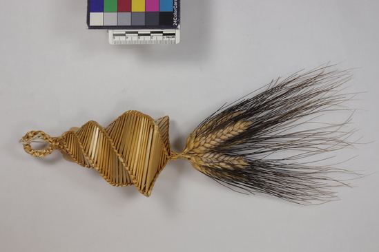 Hearst Museum object 2 of 2 titled Corn dolly, accession number 7-5910, described as Corn dolly; wheat straw, plaited; conical shape; square closed bottom with tuft of black-bearded wheat heads hanging from the center; braided loop at top; length 29 cm.