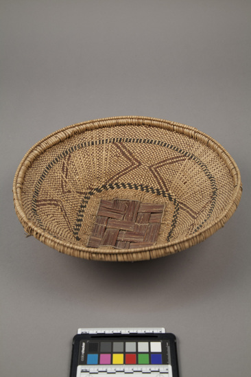 Hearst Museum object titled Basket, accession number 5-17000, described as Round, carrying basket w/ square base.  Woven in alternating brown warp/natural weft weave, decorated with chevrons of brown and bands of alternating black and natural.  1992