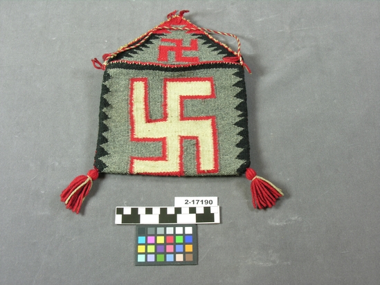 Hearst Museum object titled Bag, accession number 2-17190, described as Bag made from "Navajo" blanket; black and grey with red-outlined white swastika on bag, red swastika on flap.  Custom woven textile.