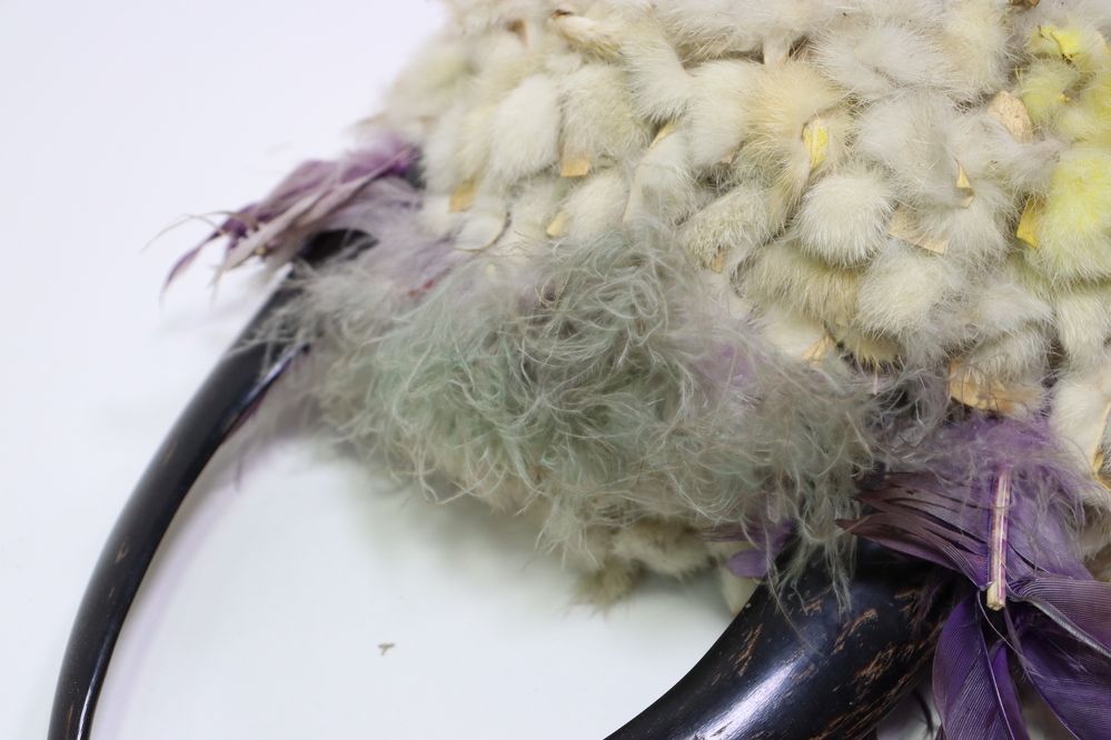 Hearst Museum object 4 of 15 titled Headdress, accession number 2-45410, described as Felt cap covered with strips of rabbit fur, patches stained yellow, traces of green fluff at front. Crown with 2 split polished horns attached to interior hide strip. Purple feathers and green-gray fluff in between and at base of horns. Multicolored silk grosgrain (?) ribbons bound to left horn tip. Ten "ermine tails" of rabbit fur sewn about a cord, red felt seized, with black hair tips; fringes at sides.