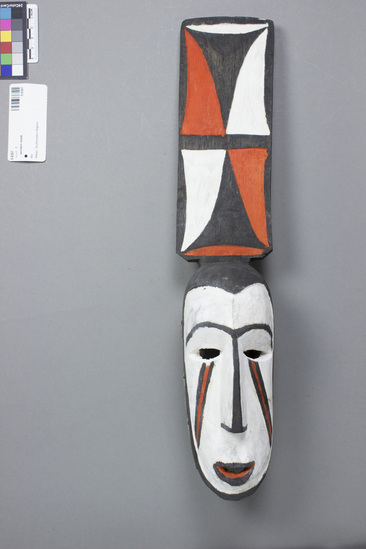 Hearst Museum object titled Mask, accession number 5-6307, described as Mask; wood; spatula-shaped ornament as part of head painted in two repeated panel designs of orange, black and red; face white with black border; eyebrows, nose and lip  outlined in black; orange and black face markings; orange inner mouth; raffia base and on back. Height 47 cm. Used for yearly (January-February) “Lubhulu” display. Used by men.