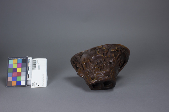 Hearst Museum object titled Cup, accession number 9-20542, described as Libation cup, rhinoceros horn, handcarved; base of horn is rim of cup; polished finish; multiple groups of men in various poses carved into sides in medium relief; open work trees carved into sides; sides flaring inward to base; H 8.2 cm X L 15 cm X W 9.1 cm