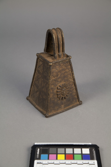 Hearst Museum object titled Bell, accession number 5-3360, described as Rectangular, truncated, brass bell with strap handle. Geometric all-over design. Height: 7.0 inches.