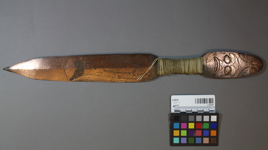 Hearst Museum object titled Knife, accession number 2-34378, described as Hammer copper knife with blade and handle a single flat piece. Leather and string are wrapped around the handle in a narrow area 10.5 cm from the round end. There is a head design stamped on each face at the end, and a fish form on one face of the blade. Figure on handle identified as shark. Polyhedral cross-section.