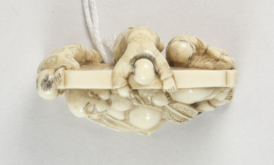 Hearst Museum object 8 of 14 titled Netsuke, accession number 9-18870, described as Netsuke; reclining figure of fat man facing to his right, supporting head on right hand; lying in front of wall; boy at left peering at man; boy at back of wall standing on barrel pulling at kimono cord; boy at right tugging at kimono hem; man holding fan in left hand; both sides of wall visible; H 3.6 cm X L 4.8 cm