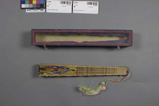 Hearst Museum object titled Fan, accession number 9-17804a,b, described as fan with case; a) fan; carved and pierced sandalwood, paper with painted court figures in bright yellow, blue, green, and orange, reverse with dark pink background, same scene; cord with pink and green tassel; b) case; box with blue cloth covering and glass lid; early 20th century