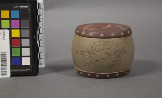 Hearst Museum object 2 of 4 titled Vessel with lid, accession number 9-22644a,b, described as ceramic vessel with lid; ceramic jar shaped like a drum inscribed with a rural scene and calligraphy around the body of the vessel (a).  red-brown band around bottom decorated with small "nail head" roundels every 1.3cm.  lid (b) red-brown with edge finished with "nail heads".  top inscribed floral design, scratched in after glaze was applied.