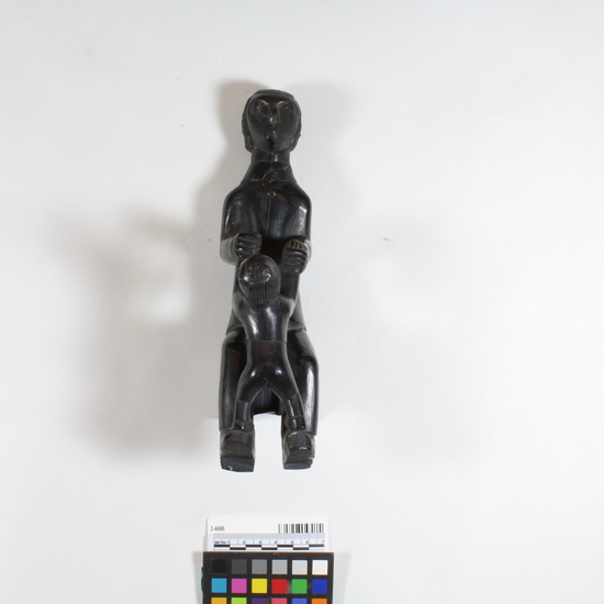 Hearst Museum object titled Statuette, accession number 2-4686, described as Argillite statuette representing white man (possibly missionary) playing with child.  Man seated on chair holding boy's hands, boy's feet on top of man's feet.