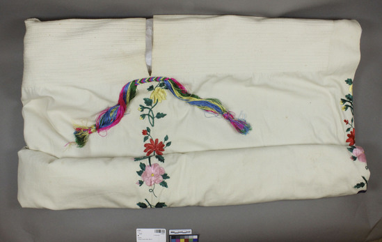 Hearst Museum object titled Huipil, accession number 3-15811, described as Huipil. White cotton warp face; raised wefts on shoulders; line of varicolored silk floral embroidery front, back, sides; silk cord and tassels across bottom of neck opening. Length 35 inches.