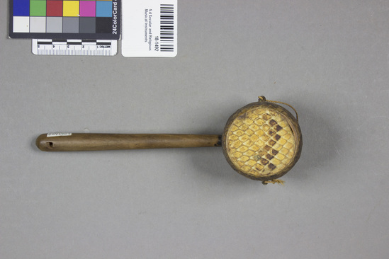 Hearst Museum object titled Rattle, accession number 18-1492, described as Rattle. Wood, snakeskin cover on ends of drum shaped head, small metal loops with remnants of cotton string on sides; handle has a hole at end. length - 17.5 cm.; head, diam. - 4.4 cm. Collector states that specimen is "a vendor's rattle.