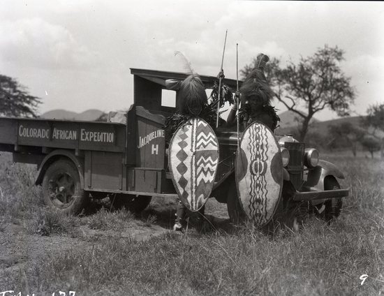 Hearst Museum object titled Black and white negative, accession number 15-32248, described as 4" x 5" Negative. Two Ikoma warriors pose with expedition truck near Lake Victoria.  Hoefler's original description: "Photo made near Lake Victoria and are of the Ikoma Tribe. They had agreed to spear the lions for us, but the Masai went to war with them and they had to stay at home to fight the Masai raiders. Quite a few on each side were killed, but it was never put in the paper as the English always cover up these things.