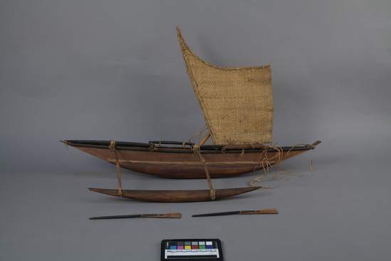 Hearst Museum object 1 of 5 titled Canoe model, accession number 11-42741a-c, described as Model of canoe, wood, single outrigger, single lateen sail, hull and sides laced together, 2 oars, undecorated. 71.0 cm.