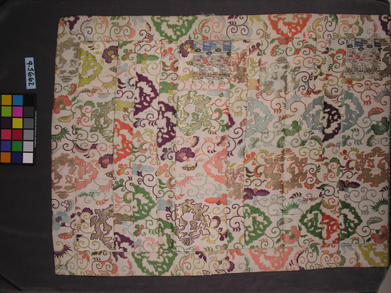 Hearst Museum object titled Robe, accession number 9-5662, described as Robe worn by Buddhist priest;  border and portion of center multicolored silk and gold brocaded on white ground; several interior strips of multi colored silk and gilt-paper brocaded on white satin ground with design of interlocking medallions enclosing dragons and birds; 2 squares plain weave brocade; 4 corner squares have been removed; pink silk lining; 107 x 188 cm