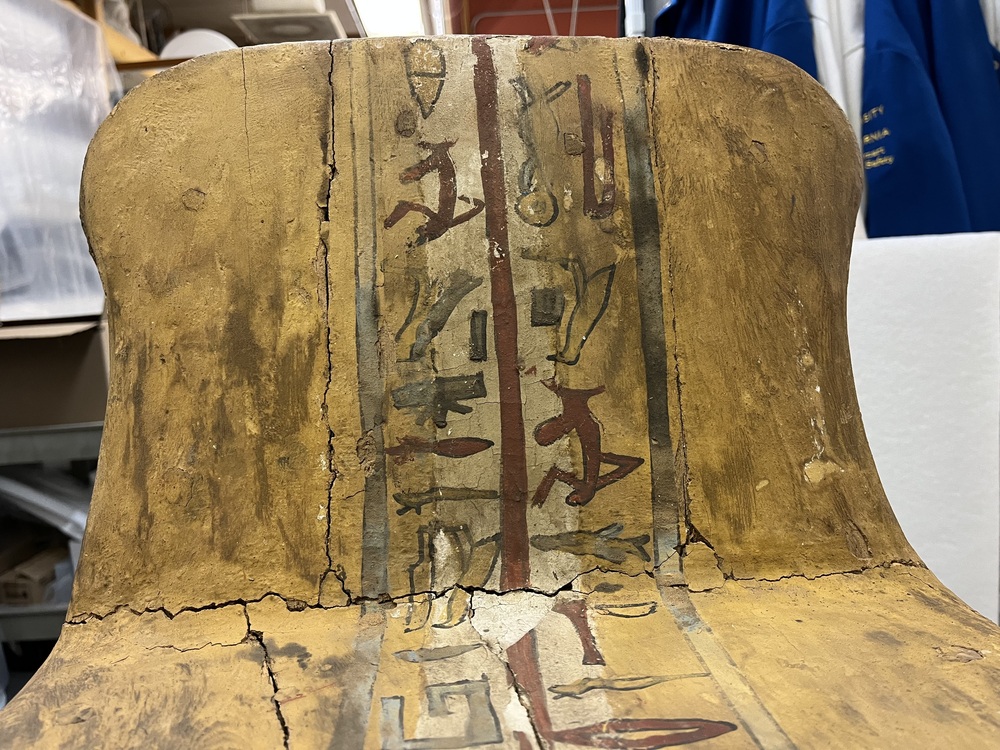 Hearst Museum object 81 of 167 titled Coffin, accession number 6-19912, described as Wooden anthropoid coffin. Inscription running down center of lid. Determined by Kea Johnston to probably be the outer coffin of Iwefaa (6-19928, 12-11039). According to Kea Johnston, "This coffin belonged to a man named Iwefaa, whose name is inserted in the middle of the spells written in the two columns on the front. This coffin is likely the outer coffin for PAHMA 6-19928 based on the similarity of the owner's name, unusual costume, and the paleography of the inscription. Both coffins were purchased on the antiquities market by George Reisner for Phoebe A Hearst. However, stylistically, they are very similar to a set of coffins known to have come from the site of Akhmim, which was excavated in the 1880s by Gaston Maspero, and which has heavily looted for the antiquities market during this decade." "The pectoral vignette between the text and the collar shows the deceased standing before squatting baboon and is the source of our logo. The hieroglyph for 'sky' is above their heads, and the side borders are formed by a pyramid and the symbol for the West.