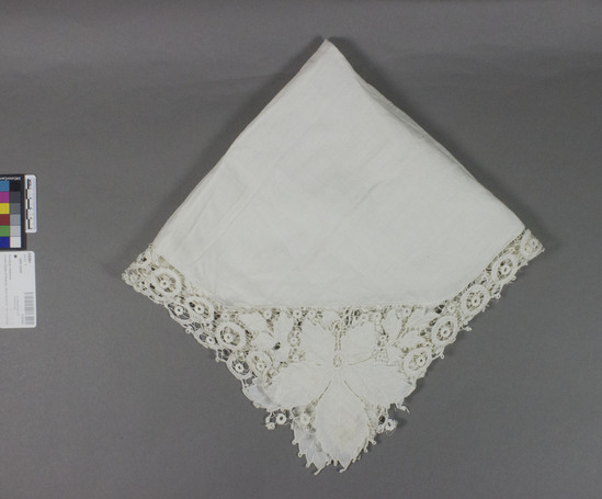 Hearst Museum object titled Table cover, accession number 2-62961, described as Table scarf. Cotton. Plain weave center; cut work and embroidery edges. White. Center cloth is an octagon, with one hole, several stains, and traces of a floral pattern that was probably intended to be embroidered; edges have wheel motives; large leaf motives at each corner