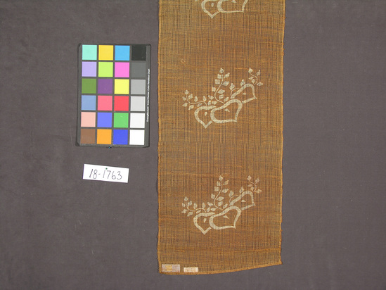 Hearst Museum object titled Textile panel, accession number 18-1763, described as Vegetable fiber panel in spaced plain weave; brown ground with stenciled or printed ecru floral motif with blossom and vine-like branches; panel is hemmed at one end with a rod casing at the other.