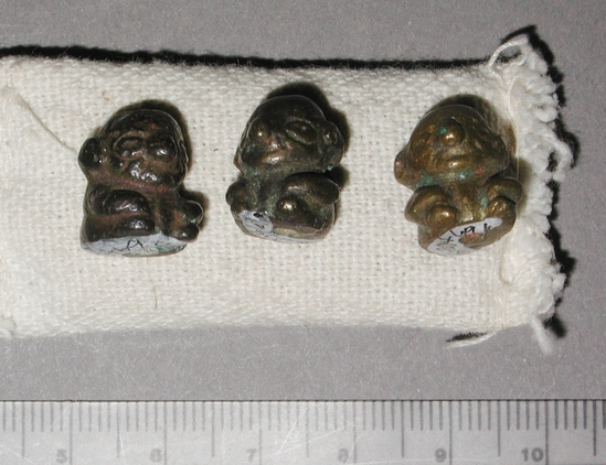 Hearst Museum object titled Beads, accession number 16-20469a-c, described as 3 bronze (?) beads in the shape of a squatting man, with large head and small squat body with hands resting on knees.  heads have large ears and nose, wide eyes, small mouth and a bald pate.  bead hole runs from top of head through base.