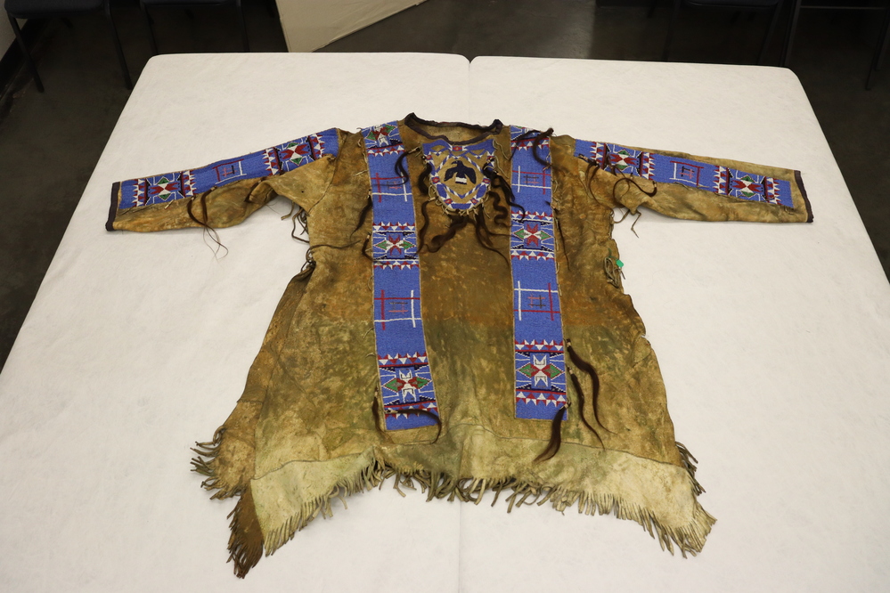 Hearst Museum object titled Shirt, accession number 2-59149, described as Buckskin; strips of multi-colored glass "seed" beads with blue background; dark blue and white bead "thunderbird" central motif front and back; scalplocks held with yarn (some detached).