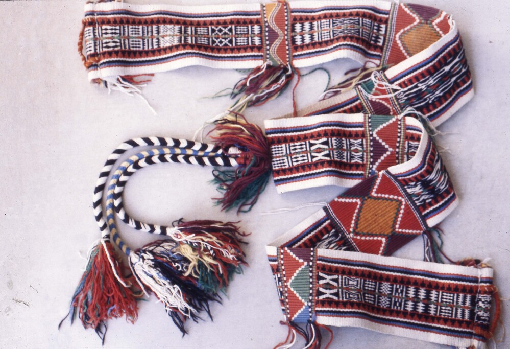 Hearst Museum object titled Color slide, accession number 25-25145, described as 35mm color slide transparency: "Cunninghams camel ornament 'malabbah'". Long woven object with striped, triangle, and diamond patterns; featuring tassel detailing; colored red, orange, green, blue, black, and white.