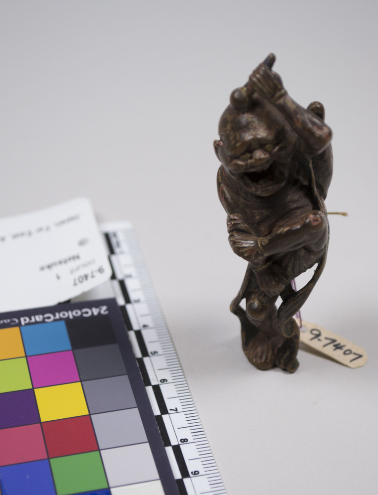 Hearst Museum object titled Netsuke, accession number 9-7407, described as Netsuke: dancing male figure, laughing grotesquely. Right hand on thigh, left hand holds dum-dum balls and strikes head.