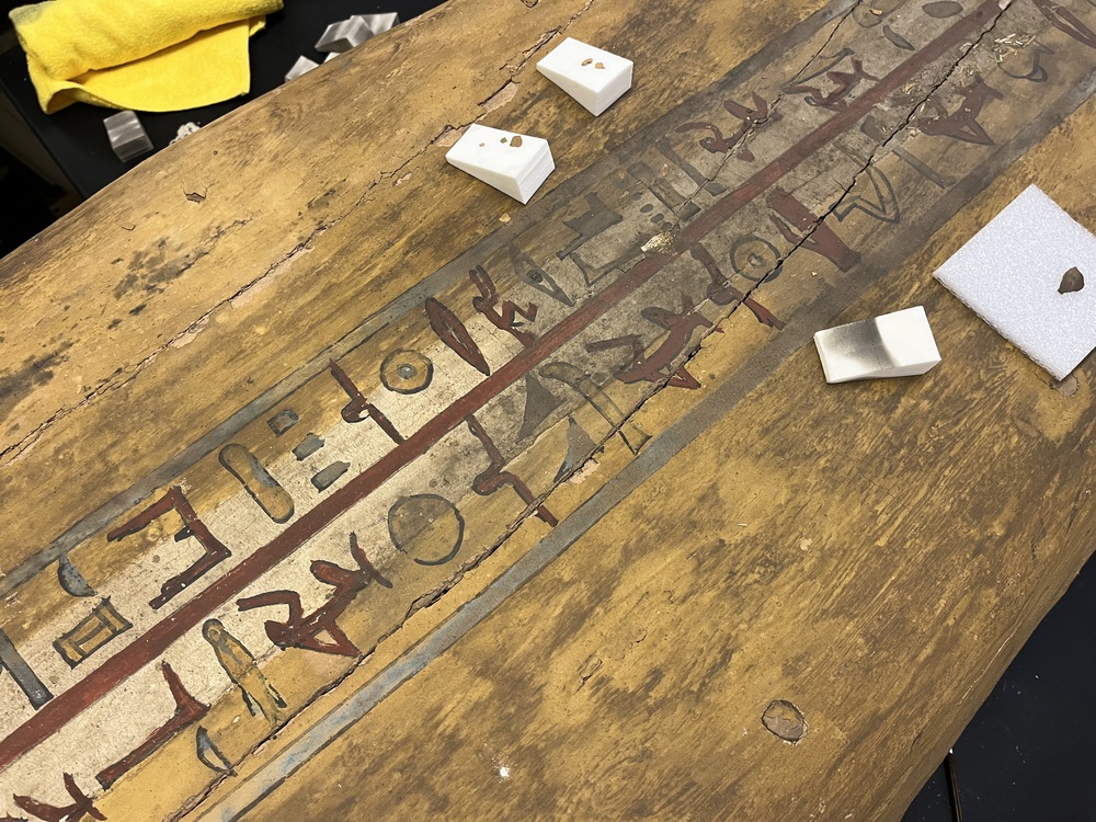 Hearst Museum object 21 of 167 titled Coffin, accession number 6-19912, described as Wooden anthropoid coffin. Inscription running down center of lid. Determined by Kea Johnston to probably be the outer coffin of Iwefaa (6-19928, 12-11039). According to Kea Johnston, "This coffin belonged to a man named Iwefaa, whose name is inserted in the middle of the spells written in the two columns on the front. This coffin is likely the outer coffin for PAHMA 6-19928 based on the similarity of the owner's name, unusual costume, and the paleography of the inscription. Both coffins were purchased on the antiquities market by George Reisner for Phoebe A Hearst. However, stylistically, they are very similar to a set of coffins known to have come from the site of Akhmim, which was excavated in the 1880s by Gaston Maspero, and which has heavily looted for the antiquities market during this decade." "The pectoral vignette between the text and the collar shows the deceased standing before squatting baboon and is the source of our logo. The hieroglyph for 'sky' is above their heads, and the side borders are formed by a pyramid and the symbol for the West.