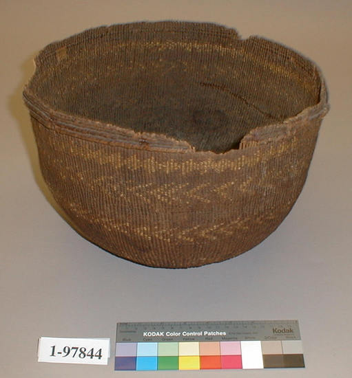 Hearst Museum object titled Cooking basket, accession number 1-97844, described as Twined, tub-shaped; 4 bands of design in Xerophyllum tenax overlay, the lower 3 are chevron bands; reinforcing row of lattice twining at rim.  Three break-outs in rim, several cracks.  Pine root weft; peeled shoot warp sticks.  Mainly plain twined.  Tag: "Wailaki attr.". Per Ralph Shanks:  Twined cooking basket, used.  Crossed warp start, not a traditional wrapped Northwest California style starting knot, it has seven plain twined rows on the exterior and interior, probably over seven warps.  See 1-2543 for a similar start.  The warp material is a peeled shoot, possibly willow; the wefts are conifer root with an overlay design in beargrass.  Starting at the starting knot there is three strand twining for about 3/4 inch, followed by plain twining up to the one row of lattice twining over a large rod, which is natively repaired in at least one area; after the lattice twining there is two rows of three strand twining followed by two rows of plain twining.  The rim is trimmed with no warp sticks protruding.  The basket somewhat undulates.  The work direction is to the right, with an exterior workface and up to the right slant of weft twist.  The overlay is irregular double sided, with the main design on the exterior.   The basket was attributed to the Wailaki by Larry Dawson based on a comparison with 1-12121, but if one looks at 1-2543, which is Lassik, there is enough similarities to bring an absolute attribution to Wailaki into question.  The basket is probably then either Wailaki or Lassik.