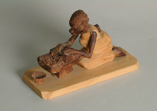 Hearst Museum object titled Thorn carving, accession number 5-16245, described as thorn carving: woman kneel before a mortar grinding material. infant on back small bowl sits in front of mortar on rectangular base.