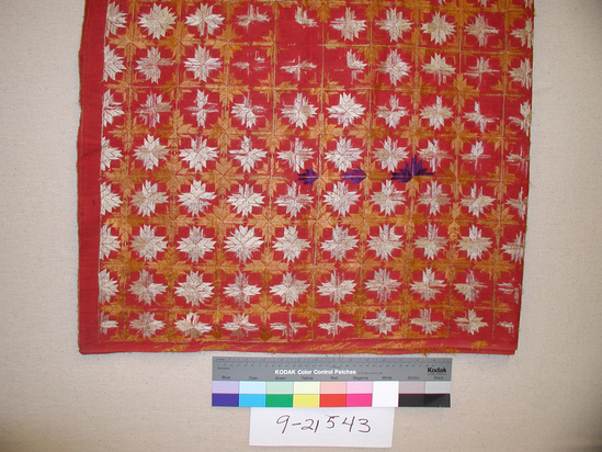 Hearst Museum object titled Textile, accession number 9-21543, described as Embroidered Cloth; L=260cm x W=131.5 cm; red ground embroidered with off-white, orange, and gold geometric shapes (stars) on light green fine grid; 2 pieces of fabric (L=80 cm and W=51.5 cm) sewn together along length; silk floss embroidery; 3 areas of deep blue-violet patterned embroidery in one corner; worn away orange embroidered pattern along selvedge.