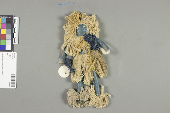 Hearst Museum object titled Doll, accession number 5-14405, described as Doll, male, Devil Dancer. Blue leather, stuffed, knots of string for eyes, clothes of tan string, anklets, kilt, neckruff (also with blue string), and headdress. Carries white whisk in left hand and blue one in right hand. Height 18 centimeters.