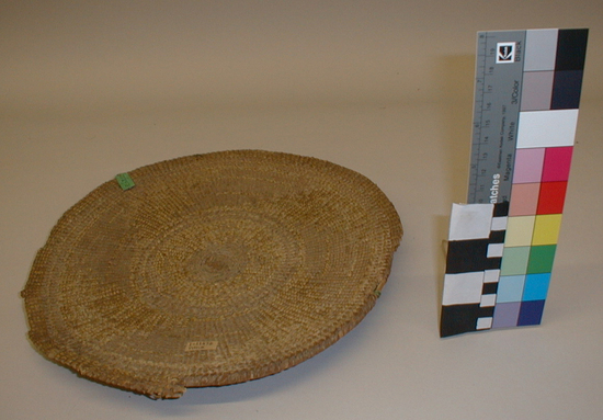 Hearst Museum object titled Sifting tray, accession number 1-11672, described as Sifting tray basket; twined. Warp is peeled Hazel (Corylus cornuta californica), weft is Sugar pine (Pinus lambertiana). White pattern is Beargrass (Xerophyllum tenax). Grimy from use. About one quarter of rim is broken off to outer lattice - twined rows. Plain twined. White overlay floated on back. 2 rows of lattice twined rods near edge and center (rods on back).