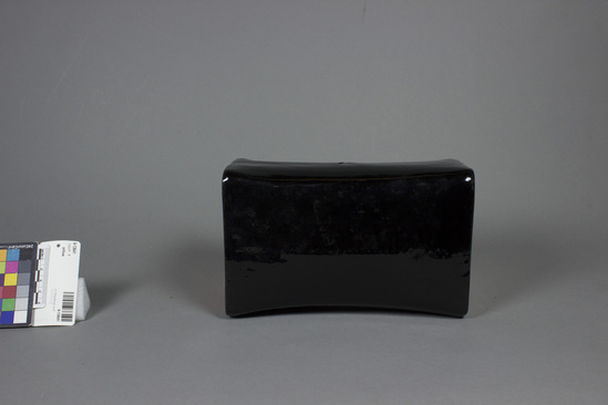 Hearst Museum object 3 of 3 titled Pillow, accession number 9-13641, described as Pillow; lacquer; black, ends painted gold with tracing of trees in black; length 20.5 cm, 13 cm x 9 cm at end. China, Hong Kong (from Mainland China, Fukian att.) Native name:  Cham tau - lacquer pillow Bamboo or rattan rmature, compacted paper padding, lacquer coating For sleeping in summer.  Believed to be cooler.  From Chinese Merchandise Emporium.  Origin:  Mainland China.