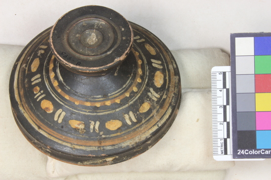Hearst Museum object titled Pyxis lid, accession number 8-995, described as Campanian Red-figure pyxis lid; intact; knob in two degrees; conical lid with downturned rim; entire lid glazed black with non-figural decoration on body: yellow and white “bead-and-reel” pattern between white and red bands, the upper bed band decoration with yellow dots.