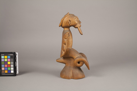 Hearst Museum object titled Figure, accession number 5-16012, described as Ashanti forest spirit : handcarved white mahogany wood; squat, with arms extended over carved wings. Square beard, horns, and looped legs. Seated on a stool-like seat. Hair carved in 3 layers. Bascom paper label on bottom.