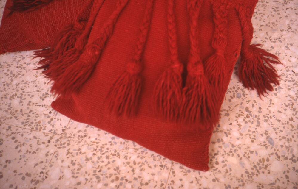 Hearst Museum object titled Color slide, accession number 25-98595, described as 35mm color slide transparency: "pillows made from saddle blanket". Close-up of red textile with tassel detailing.