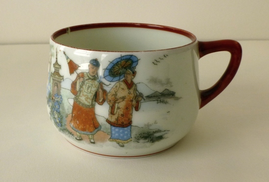 Hearst Museum object titled Cup, accession number 9-23478, described as A colored decal of a man and a woman, each with an umbrella, walking in a picturesque landscape. Elements of Chinoiserie. On the reverse a smaller colored decal shows a man carrying a woman in a basket on his back. Red ring on the interior rim, red glaze completely covers the handle and around the foot.