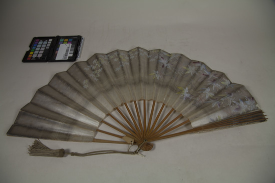 Hearst Museum object titled Fan, accession number TEMP 2018.1083, described as sign says "do NOT catalogue; for exchange or school use only"; paper and wood fan with butterfly techniques on one side and maple leafs on the other; tassel attached to base