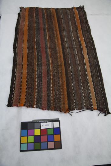 Hearst Museum object titled Tent wall or shelter wall, accession number 9-23804, described as Wall for tent or shelter, hidim, is a piece of a much longer strip. It is in natural colors - gray, brown, and white - with orange and red (faded totally) over dye in plain weave in vertical stripe and dot/horizontal stripe pattern. It was cut off a large piece because I didn't have space to bring the whole piece. Made for self and used as a windbreak. Might have been used for human shelter before their houses were built, but more likely used for goat shelters. Z-ply, commercial dye used but unsure, 10 thread count per inch. Warp-faced plain weave.