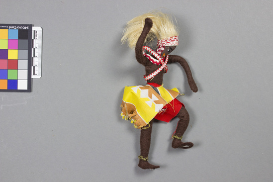 Hearst Museum object titled Doll, accession number 5-14375, described as Doll, male, Watusi dancer. Felt wire figure with painted features. Dressed in print material; skirt of red, yellow, and brown. Red and white band circling his neck and criss-crossing torso. Has a lions mane headdress and gold braid anklets. Height 15.9 centimeters. Materials: felt, wire, cotton.