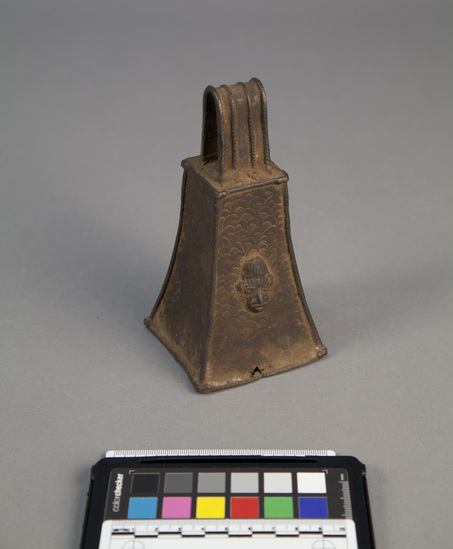 Hearst Museum object titled Bell, accession number 5-3361, described as Rectangular, truncated, brass bell with strap handle. Cross-hatched design with head on one side. Height: 6.0 inches.