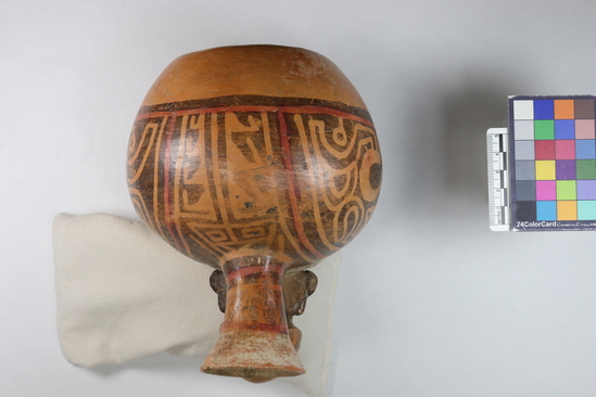 Hearst Museum object 5 of 13 titled Bottle, accession number 16-12114, described as Pottery bottle with flaring spout; effigy of a man with bag slung around neck; red and white slip and resist painted designs. Has been waxed