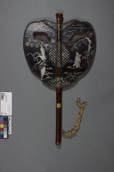 Hearst Museum object titled Fan, accession number 9-8080a,b, described as Mask-fan; Chinese; wood inlaid with figures of mother-of-pearl ad cut-outs for eyes; orange and cream silk cords from handle; 23.5 x 41.9 cm. Native name and meaning: Kazashi or benmen, convenient mask fan. a- fan, b- bag