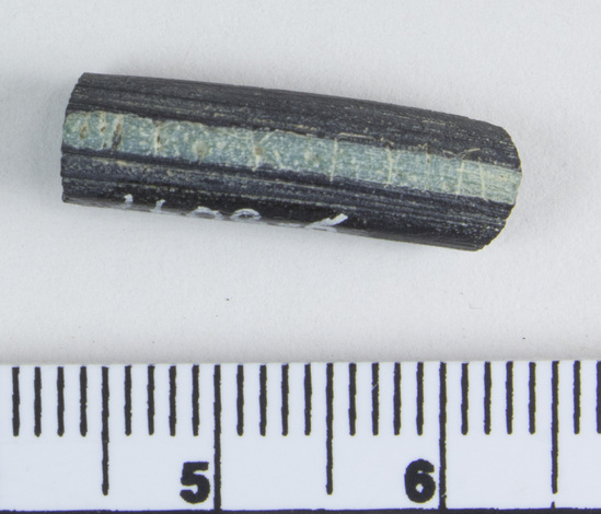 Hearst Museum object 6 of 6 titled Bracelet fragment, accession number 9-8047, described as Glass bracelet frag.; opaque black, curved rod w/ pale blue-green longitudinal bands; 20 x 6 mm.