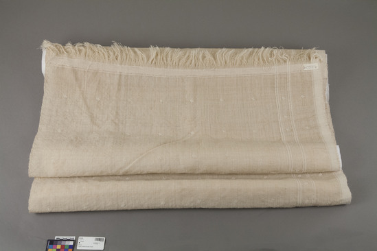 Hearst Museum object 2 of 2 titled Shawl, accession number 9-21229, described as Shawl.  211 cm. long x  91.5 cm. wide; ecru (natural) hemp (?) (single-ply) plus some natural cotton warp on one selvedge only (3 cm. wide) + 2 double stripes.  Yarn appears handspun (irregular in diameter).  Cotton weft stripe 3.5 cm. at each end before fringe ends.  Fringes are 6-7 cm. long.  Scattered cotton embroidery all over:  3 lines forming a parallelogram, spaced 13 cm. apart (length) x 11 cm. apart (width), each motif measures 1.2 x 1.7 cm.; embroidery appears to be close running stitch.