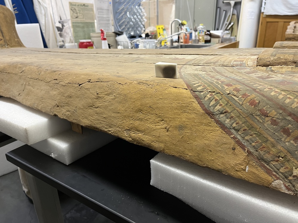 Hearst Museum object 157 of 167 titled Coffin, accession number 6-19912, described as Wooden anthropoid coffin. Inscription running down center of lid. Determined by Kea Johnston to probably be the outer coffin of Iwefaa (6-19928, 12-11039). According to Kea Johnston, "This coffin belonged to a man named Iwefaa, whose name is inserted in the middle of the spells written in the two columns on the front. This coffin is likely the outer coffin for PAHMA 6-19928 based on the similarity of the owner's name, unusual costume, and the paleography of the inscription. Both coffins were purchased on the antiquities market by George Reisner for Phoebe A Hearst. However, stylistically, they are very similar to a set of coffins known to have come from the site of Akhmim, which was excavated in the 1880s by Gaston Maspero, and which has heavily looted for the antiquities market during this decade." "The pectoral vignette between the text and the collar shows the deceased standing before squatting baboon and is the source of our logo. The hieroglyph for 'sky' is above their heads, and the side borders are formed by a pyramid and the symbol for the West.