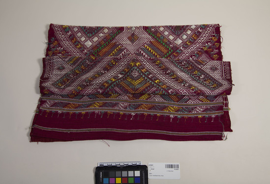 Hearst Museum object titled Shawl, accession number 9-23431, described as Shawl. Red fabric with weft stripes of white, purple, yellow and green. Most of the space between weft stripes is embroidered with geometric designs in green, white, yellow, orange and purple-grey thread.