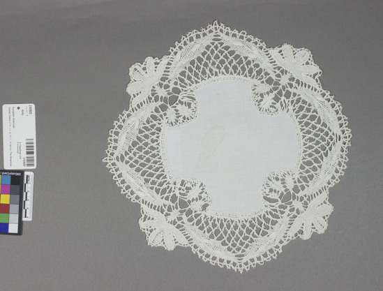 Hearst Museum object titled Doily, accession number 2-63925, described as Lace doily: white linen cross shaped center edged with coarse Cluny lace with heavy cordonnet on the four flower shapes at each side. Color: white. 11.5 inches by 11.75 inches. Good condition lace mended. Stain of linen. circa 1900.