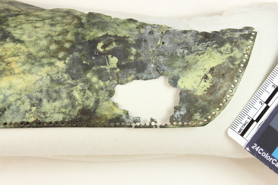 Hearst Museum object 4 of 45 titled Greaves, accession number 8-109, described as Bronze greave and 9 fragments small holes all around edge; serpent and scroll design raised and repousee; greave 41.9 cm long