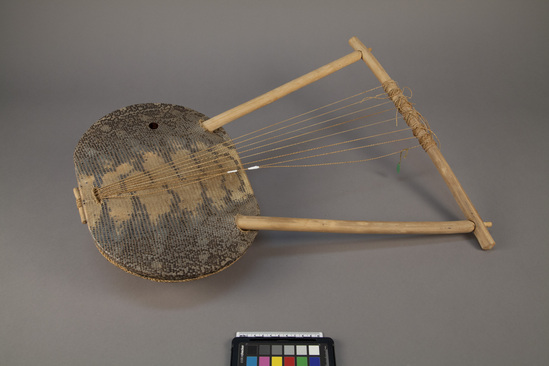 Hearst Museum object titled Lyre, accession number 5-2420, described as Bowl-lyre; 8 strings; snake-skin head laced to leather patch on back of resonator bowl; 2 arms and yoke; ca 22 inches l; bowl: 11.75 inches x 9.5 inches.